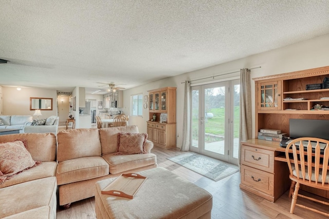 living room featuring a textured ceiling, built in desk, light wood-type flooring, and a ceiling fan