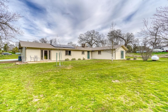 rear view of property featuring solar panels, a lawn, and a patio