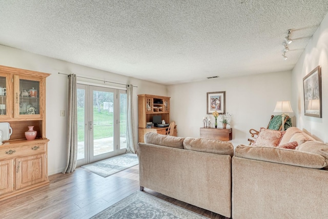 living area featuring light wood finished floors, track lighting, visible vents, and a textured ceiling