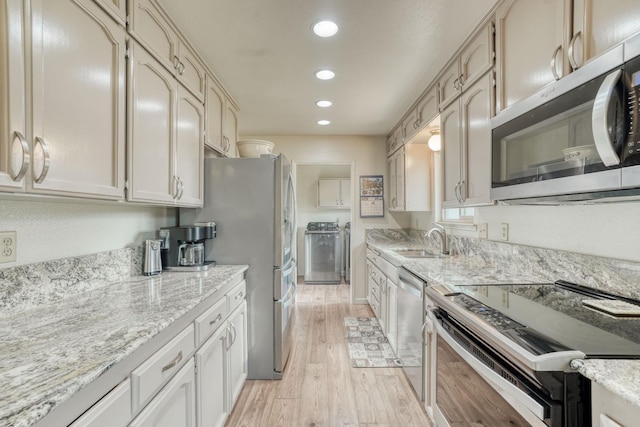 kitchen featuring light wood-style flooring, appliances with stainless steel finishes, light stone countertops, a sink, and recessed lighting