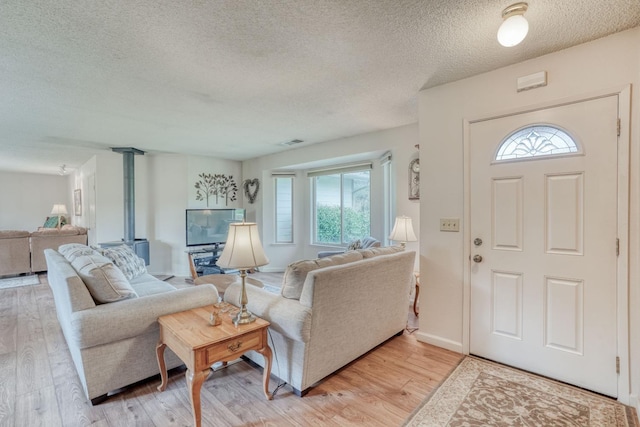 foyer entrance with baseboards, visible vents, light wood-style flooring, a wood stove, and a textured ceiling