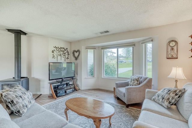 living area with a textured ceiling, visible vents, baseboards, light wood finished floors, and a wood stove