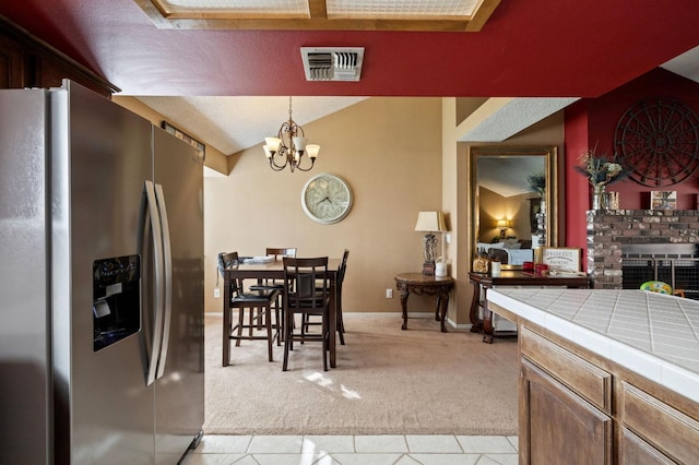 dining area with visible vents, light colored carpet, lofted ceiling, an inviting chandelier, and a brick fireplace