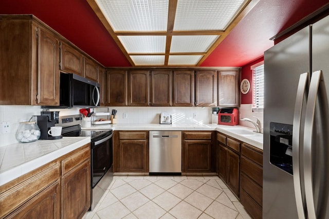 kitchen featuring tile countertops, light tile patterned floors, stainless steel appliances, a sink, and backsplash