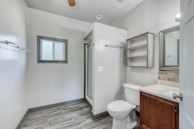 bathroom featuring a shower, toilet, vanity, wood finished floors, and baseboards