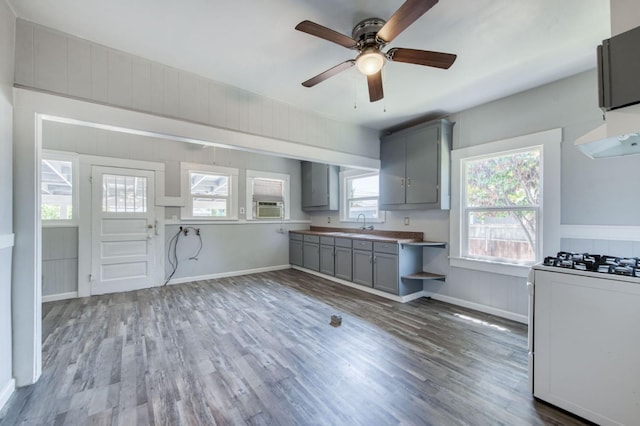 kitchen featuring baseboards, white range with gas cooktop, wood finished floors, and gray cabinetry