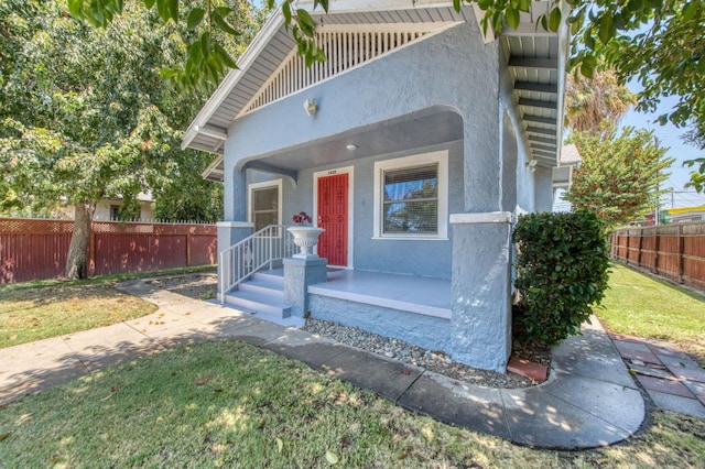 mediterranean / spanish-style home with a porch, a front yard, fence, and stucco siding