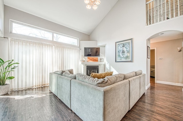 living area featuring arched walkways, high vaulted ceiling, dark wood-type flooring, a fireplace, and baseboards