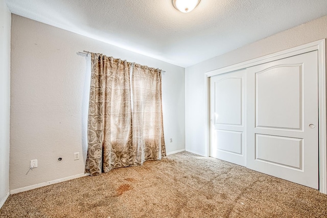 unfurnished bedroom with baseboards, a textured wall, a textured ceiling, carpet flooring, and a closet