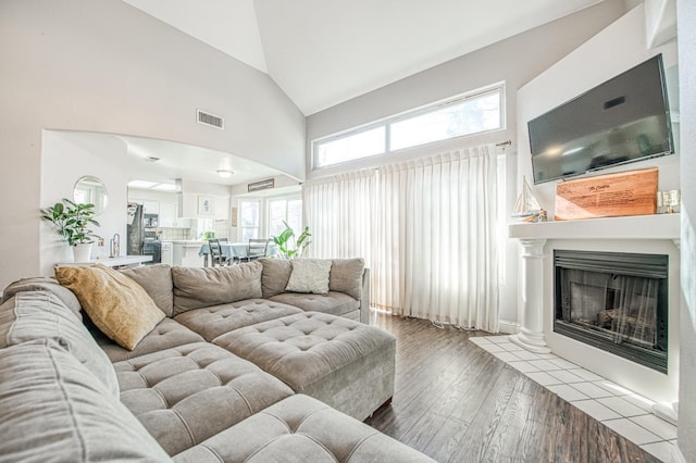 living room with light wood-style floors, a fireplace with flush hearth, visible vents, and high vaulted ceiling