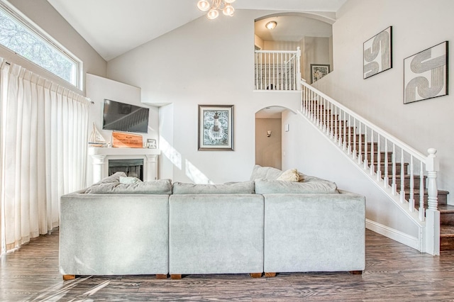 living area with arched walkways, high vaulted ceiling, a fireplace, wood finished floors, and stairs