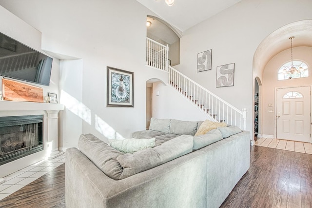 living room featuring high vaulted ceiling, a fireplace with raised hearth, stairway, and wood finished floors