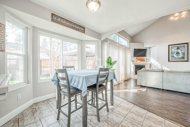 dining space with a fireplace, vaulted ceiling, baseboards, and light tile patterned floors