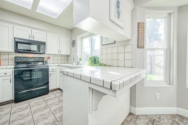 kitchen with tile countertops, a sink, a healthy amount of sunlight, white cabinets, and black appliances