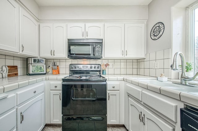 kitchen featuring black appliances, tasteful backsplash, white cabinets, and a sink