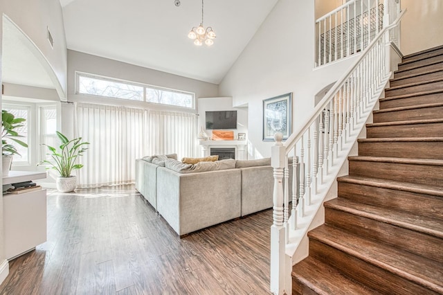 living room with high vaulted ceiling, a fireplace, wood finished floors, stairs, and an inviting chandelier