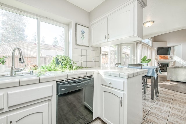 kitchen with black dishwasher, tile countertops, backsplash, and white cabinetry