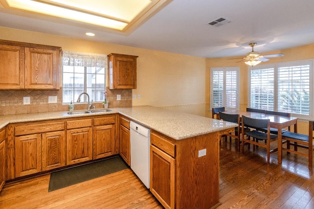 kitchen with visible vents, light wood-style flooring, white dishwasher, a sink, and a peninsula