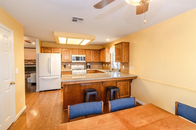 kitchen with white appliances, light wood finished floors, visible vents, a peninsula, and a sink