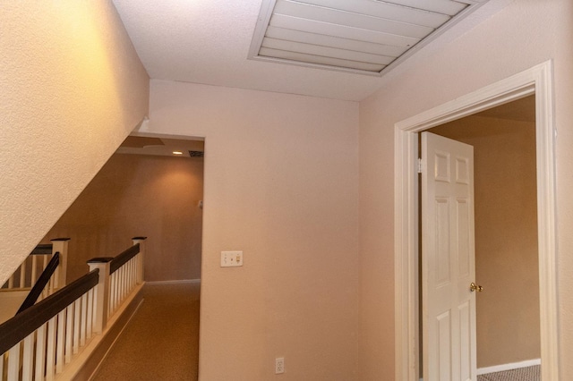 corridor with carpet floors, baseboards, visible vents, and an upstairs landing