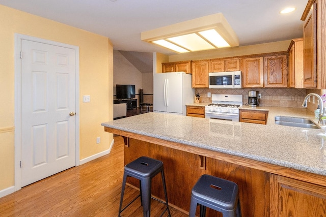 kitchen featuring a peninsula, white appliances, a sink, light wood-type flooring, and backsplash