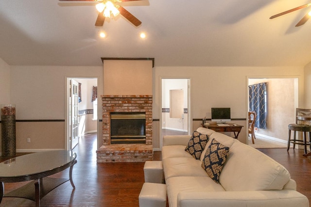 living room featuring a brick fireplace, ceiling fan, baseboards, and dark wood-type flooring