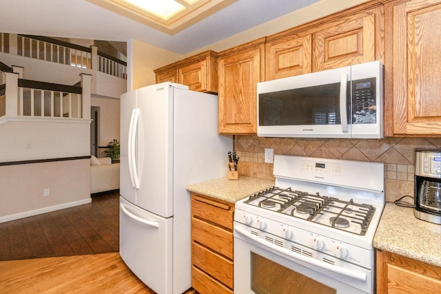 kitchen featuring white appliances, light stone counters, backsplash, and light wood-style floors