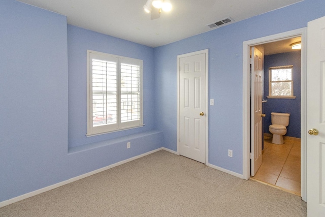 unfurnished bedroom featuring carpet, visible vents, ensuite bathroom, tile patterned flooring, and baseboards