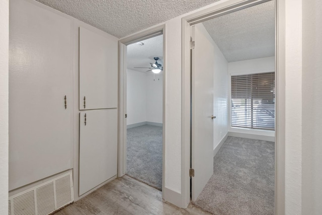 hall featuring light carpet, light wood-style floors, visible vents, and a textured ceiling