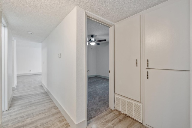 hallway with light wood finished floors, baseboards, visible vents, and a textured ceiling