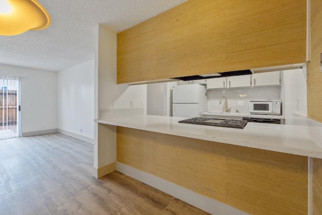 kitchen with white appliances, light wood-style flooring, a peninsula, and a textured ceiling