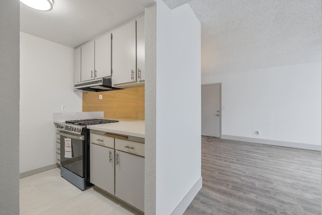 kitchen with under cabinet range hood, white cabinetry, light countertops, decorative backsplash, and gas stove