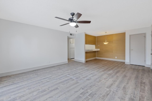 unfurnished living room featuring light wood-style flooring, ceiling fan, wooden walls, and baseboards