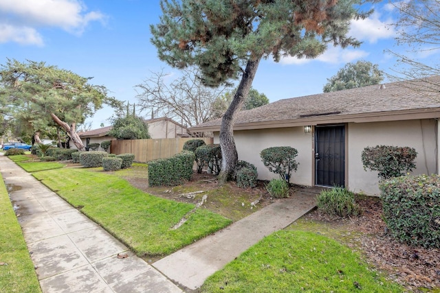 view of front of property with a yard, roof with shingles, fence, and stucco siding