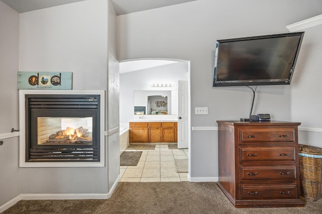 interior space with arched walkways, a multi sided fireplace, connected bathroom, and light colored carpet