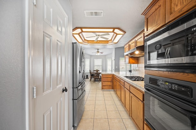 kitchen featuring light tile patterned floors, visible vents, brown cabinets, a peninsula, and stainless steel appliances