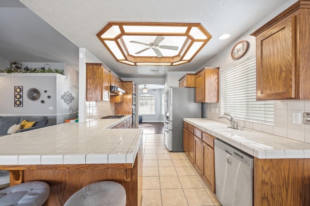 kitchen with stainless steel appliances, light tile patterned flooring, a sink, ceiling fan, and under cabinet range hood