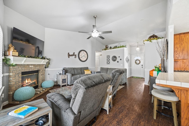 living area featuring lofted ceiling, a brick fireplace, a ceiling fan, and dark wood-style flooring