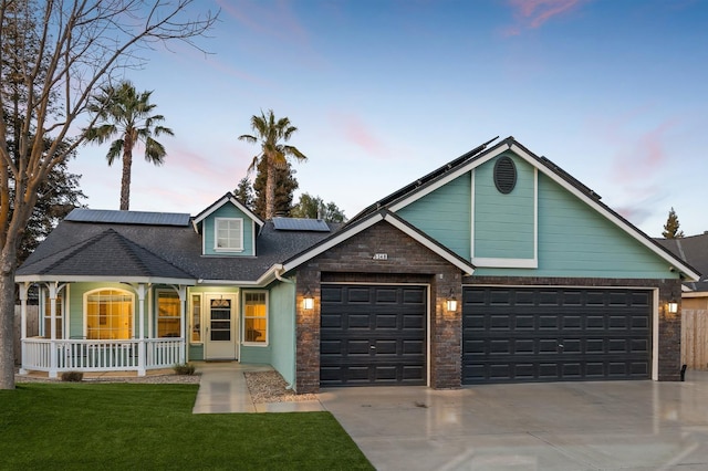 view of front of home featuring a porch, concrete driveway, an attached garage, a front yard, and roof mounted solar panels