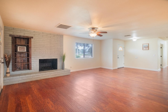 unfurnished living room featuring a ceiling fan, visible vents, a fireplace, and wood finished floors