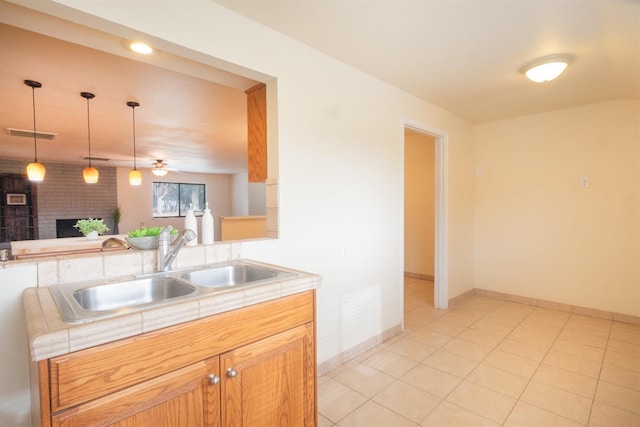 kitchen featuring light tile patterned floors, a sink, a brick fireplace, tile counters, and decorative light fixtures