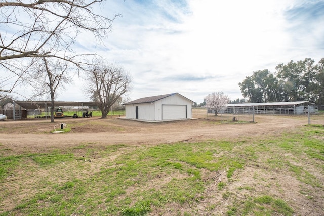 view of yard with dirt driveway, a detached garage, an outbuilding, fence, and a carport