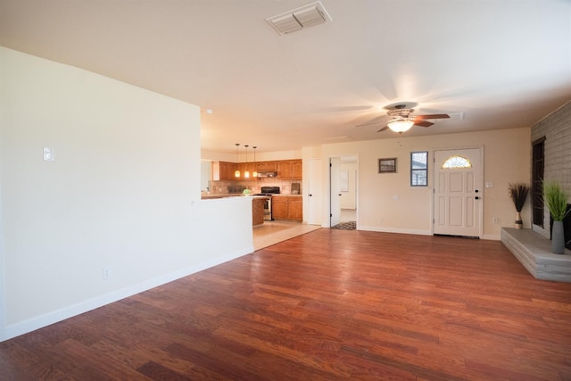 unfurnished living room with a ceiling fan, wood finished floors, visible vents, and baseboards