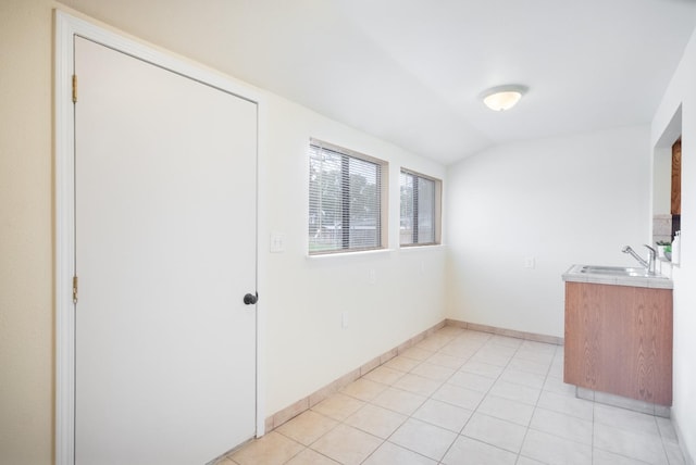 interior space with vaulted ceiling, a sink, baseboards, and light tile patterned floors