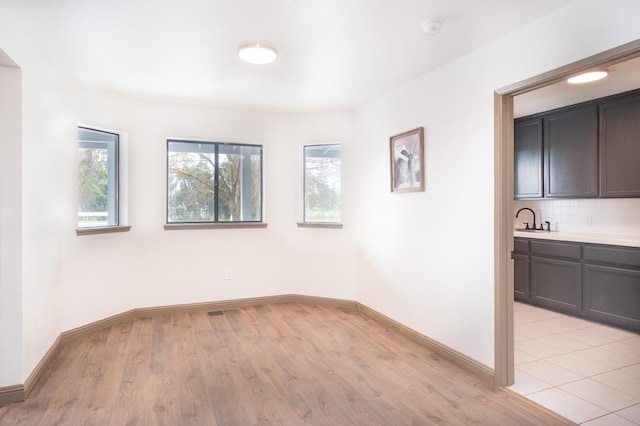 empty room with light wood-type flooring, a healthy amount of sunlight, a sink, and baseboards