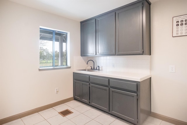 kitchen featuring tile countertops, visible vents, backsplash, gray cabinetry, and a sink