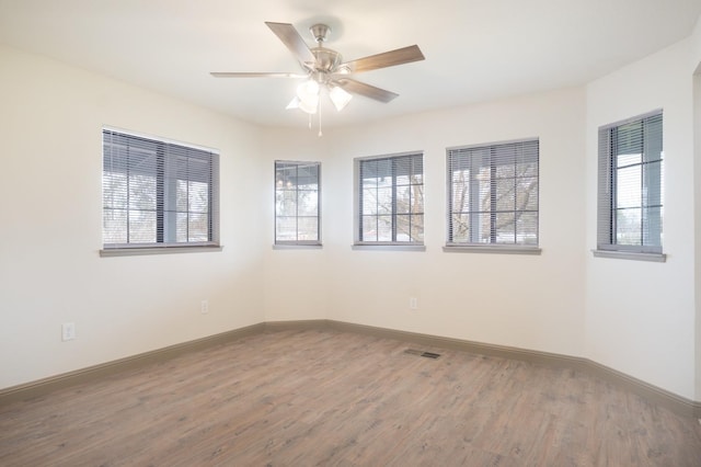 empty room with visible vents, plenty of natural light, baseboards, and wood finished floors