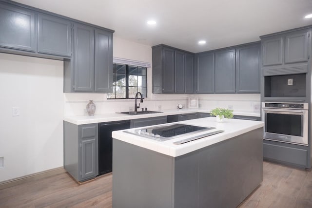 kitchen with black dishwasher, light wood-style flooring, stainless steel oven, a sink, and stovetop