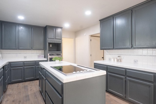 kitchen with decorative backsplash, stainless steel oven, electric cooktop, and wood finished floors