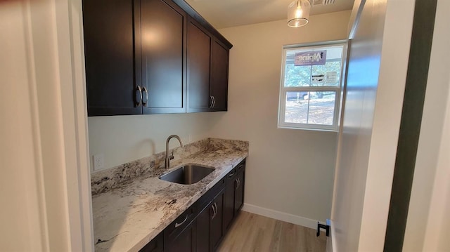 kitchen featuring a sink, light stone counters, light wood finished floors, baseboards, and dark brown cabinets